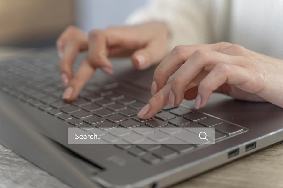 hand typing on keyboard laptop with search bar