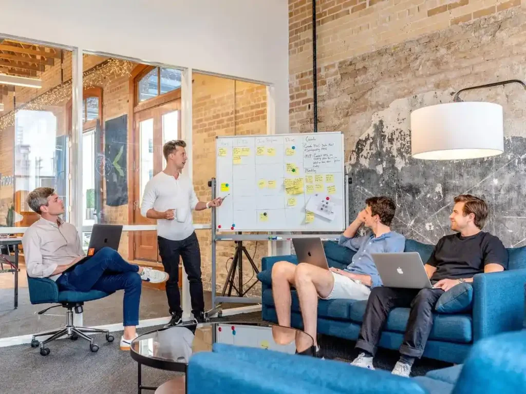 Brand Storytelling: Manfaat, Elemen, dan Strateginya 3 4 orang pegawai sedang berdiskusi menggunakan papan dan sticky note untuk menggambarkan brand storytelling