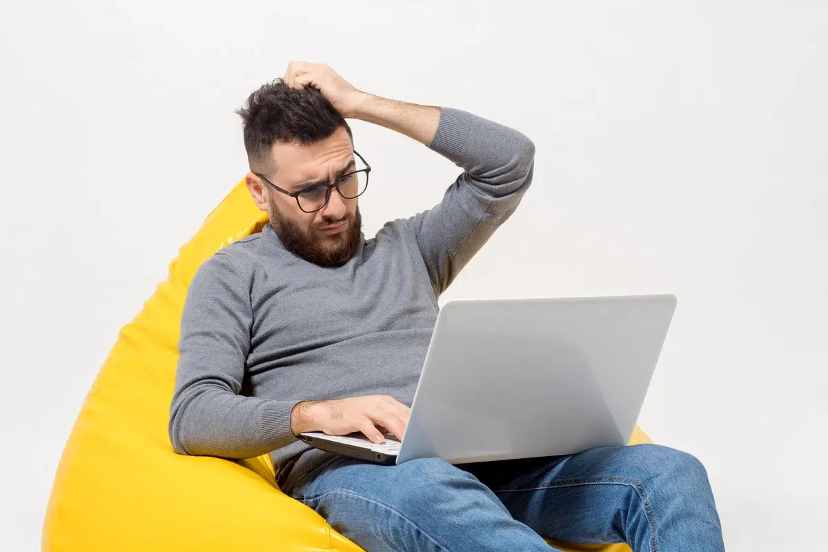 a guy feel frustated while sitting in yellow pouf chair with laptop on his hand